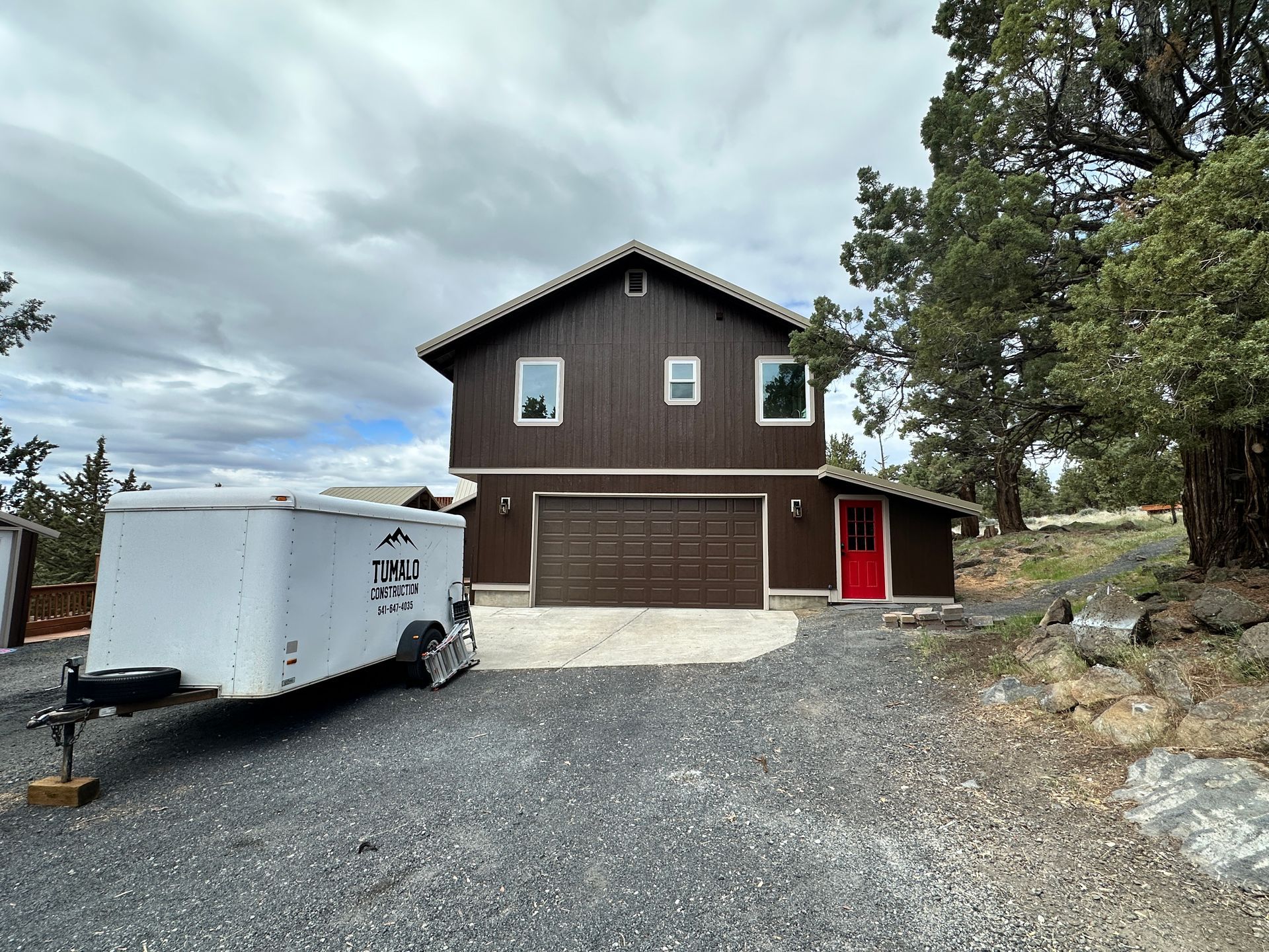 A white trailer is parked in front of a brown house.