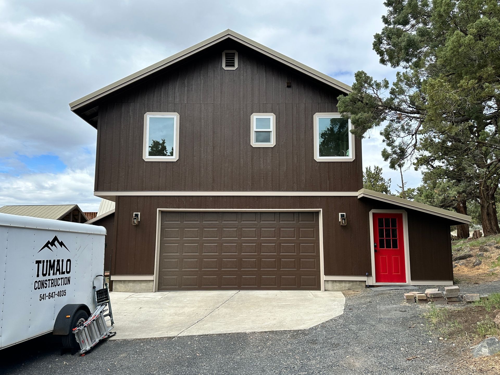 A large brown house with a red door and a white trailer parked in front of it.