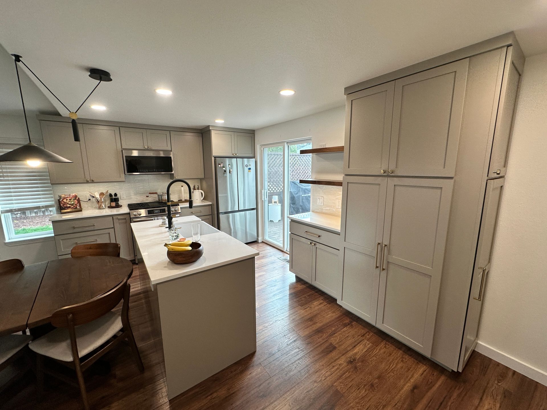A kitchen with white cabinets , a large island , a table and chairs.