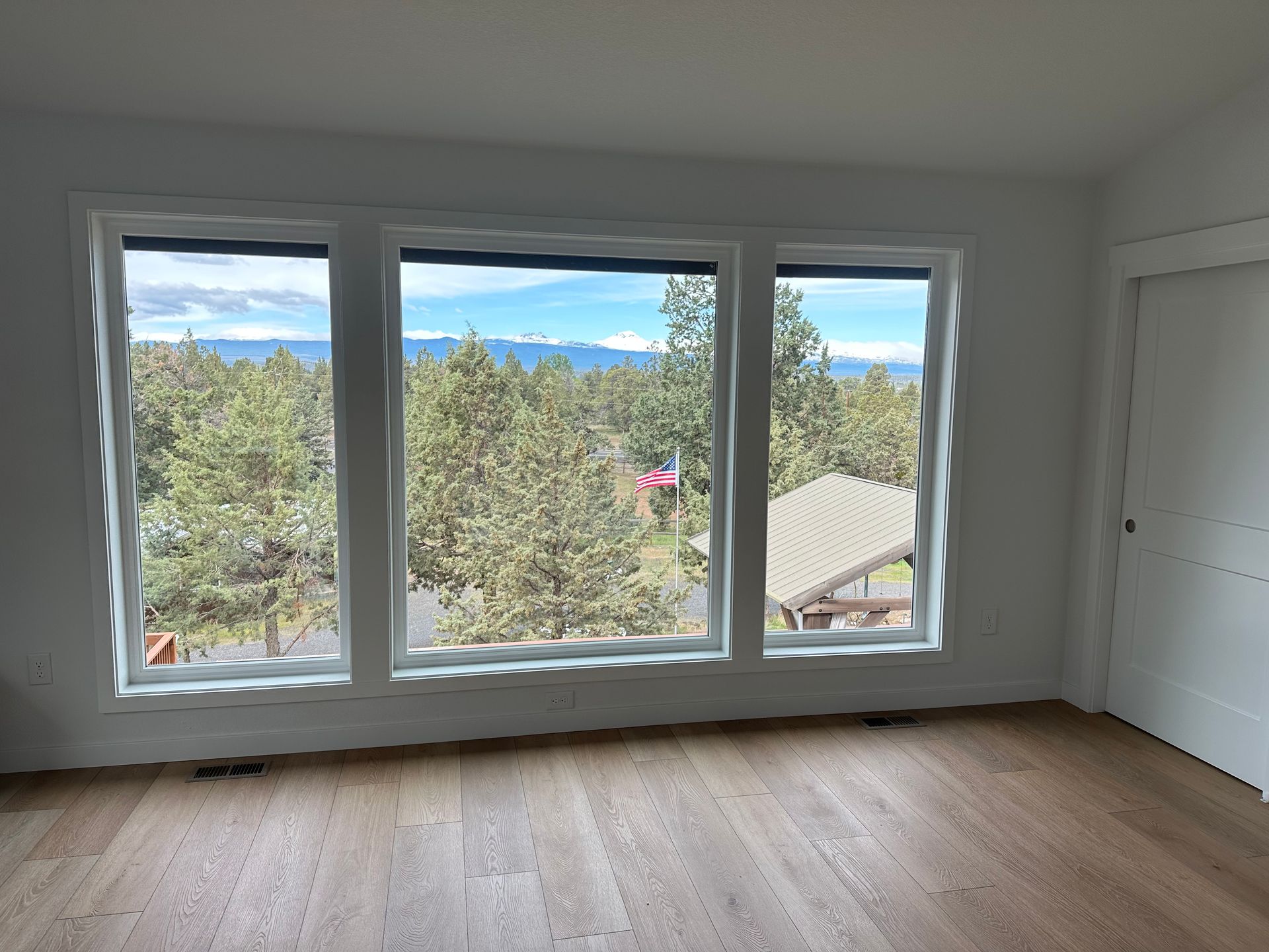An empty room with three windows and a view of a forest.