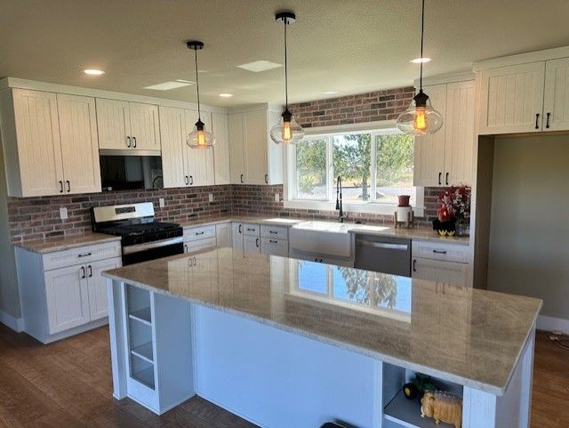 A kitchen with white cabinets , granite counter tops , stainless steel appliances and a large island.