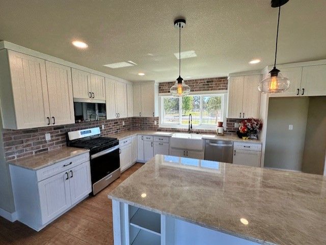 A kitchen with white cabinets , stainless steel appliances , granite counter tops and a large island.