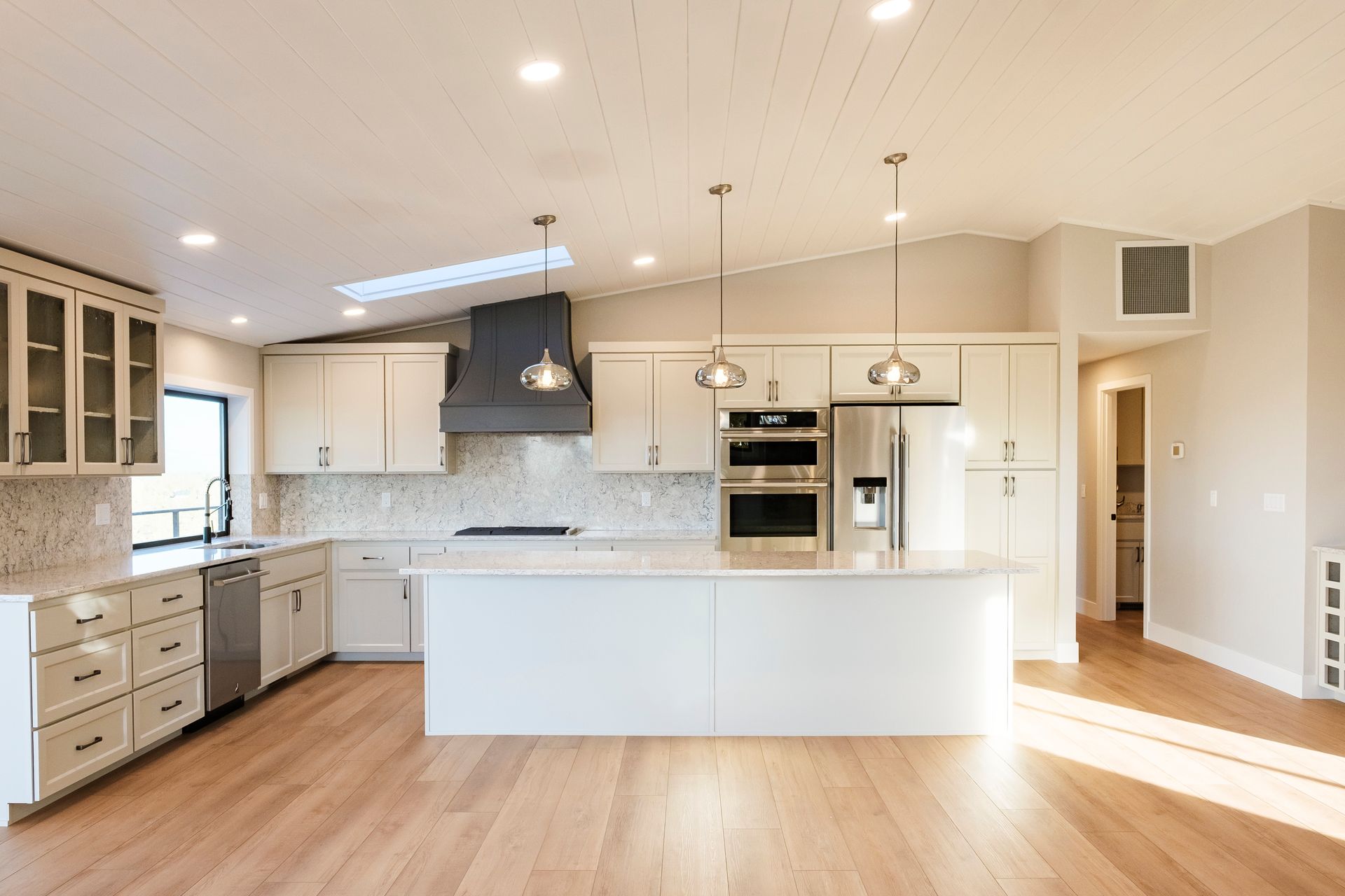 Modern white house with black trim and metal roof on a rocky cliffside, surrounded by trees.