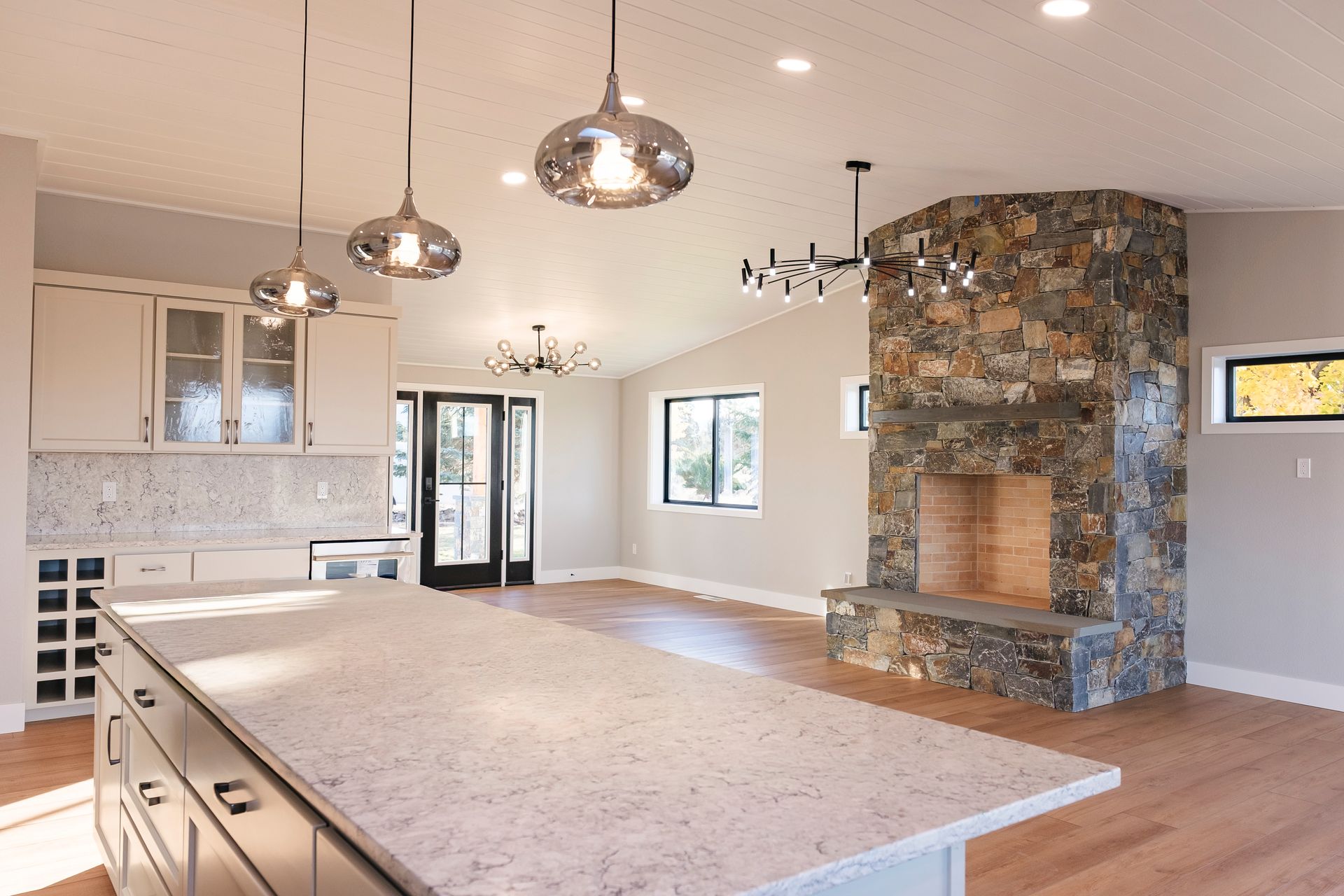 Modern kitchen with stone fireplace, island, hardwood floors, and overhead lighting.