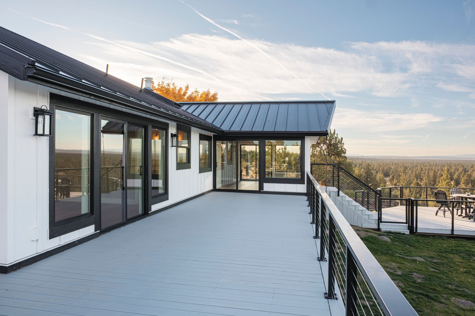 Exterior of white house with gray deck, black trim, and scenic view.