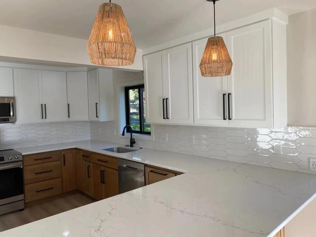 A kitchen with white cabinets , stainless steel appliances , a sink , and two pendant lights.