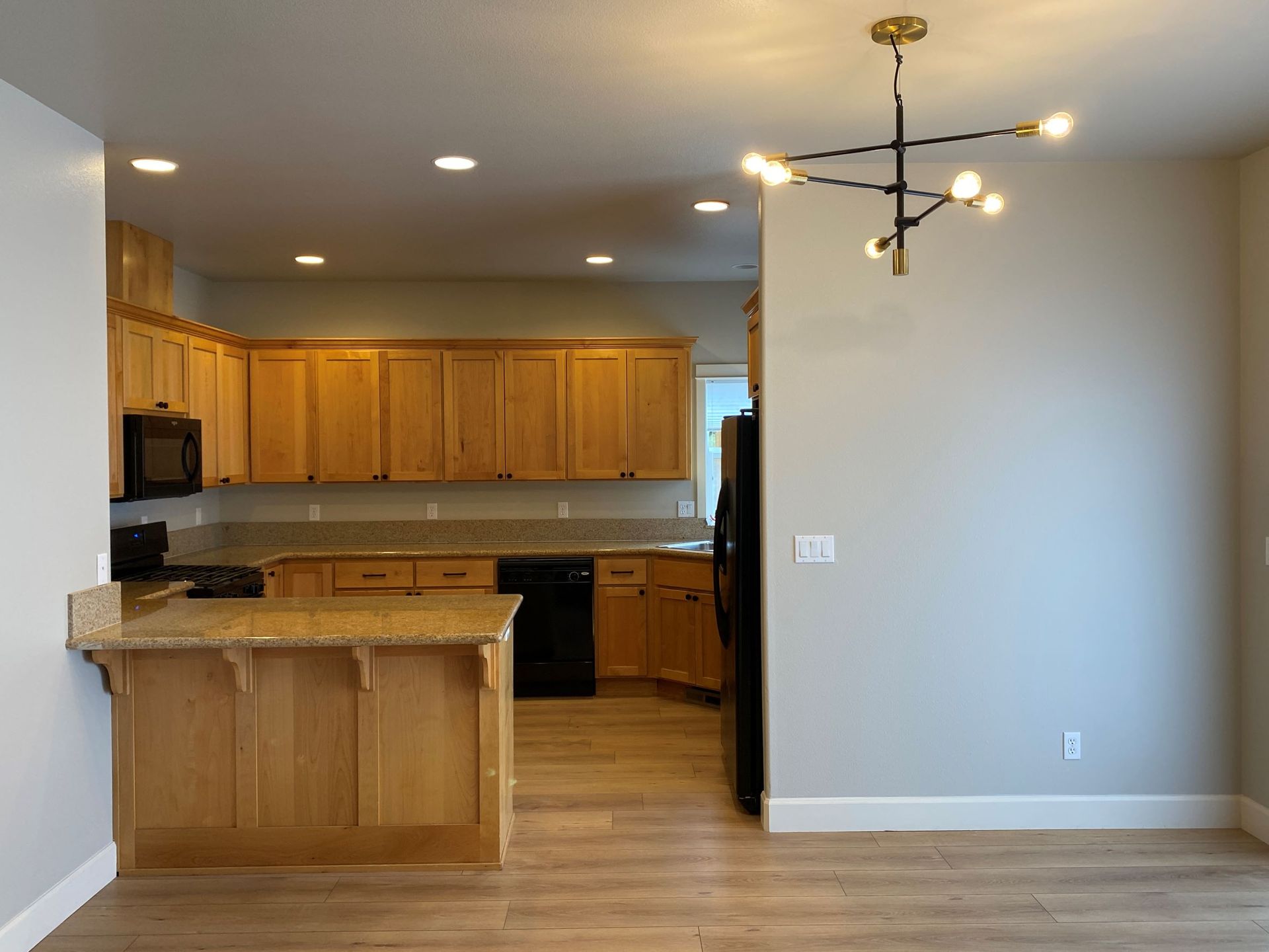 A kitchen with wooden cabinets , granite counter tops , a refrigerator and a microwave.