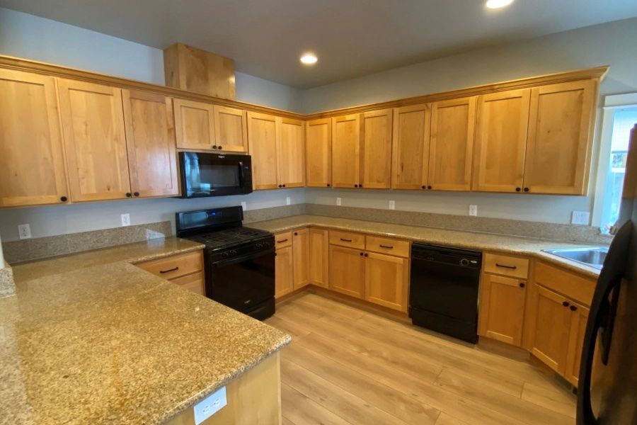 A kitchen with wooden cabinets , black appliances and granite counter tops.