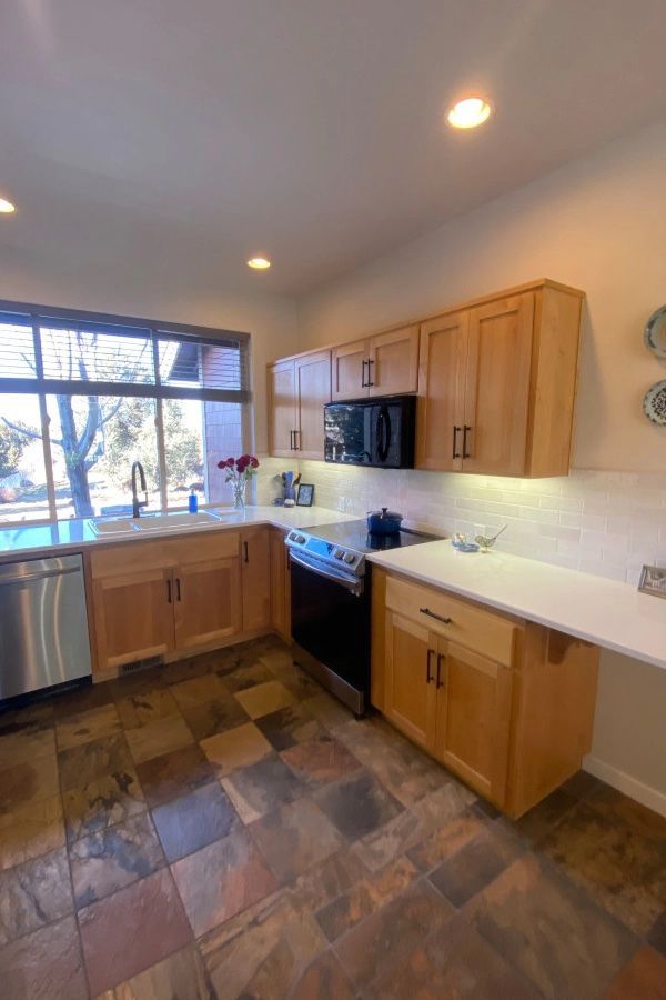 A kitchen with wooden cabinets , stainless steel appliances , and a large window.