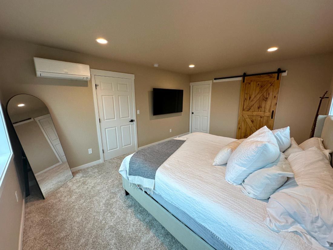 A bedroom with a large bed , television , mirror and air conditioner.
