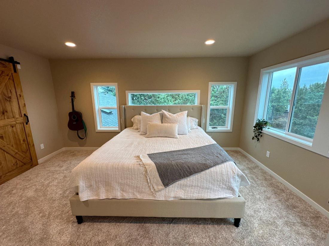There is a bed in the middle of the room with a guitar hanging on the wall.