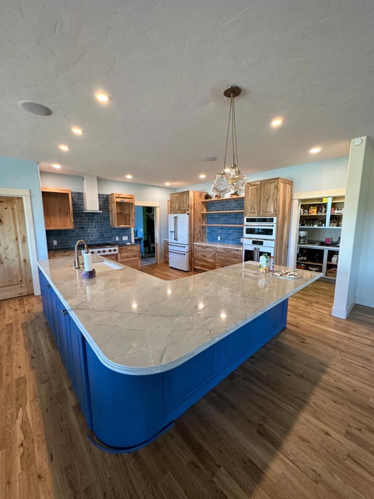 A kitchen with blue cabinets , white counter tops , and hardwood floors.