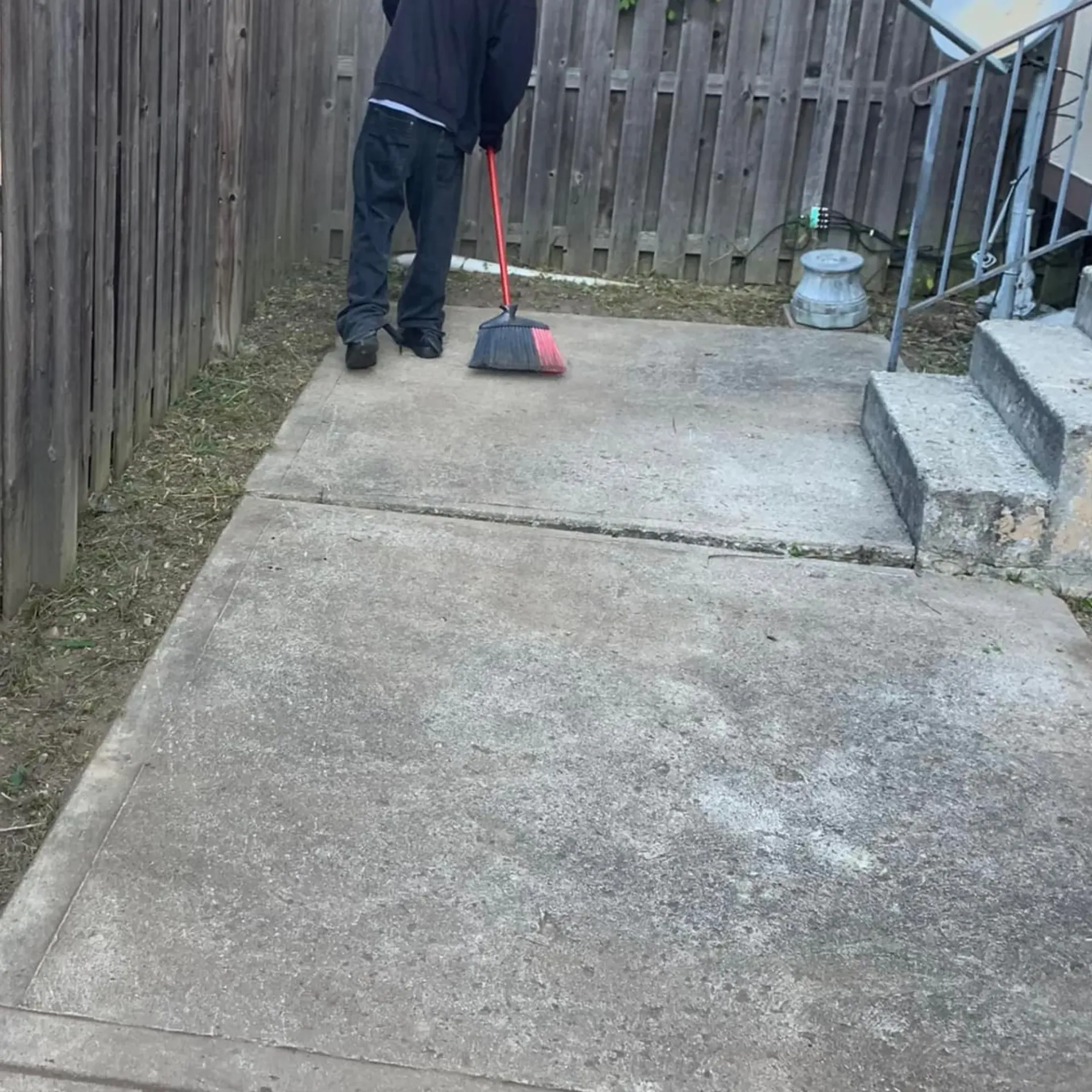 Hall's Hauling -A man is sweeping the sidewalk with a broom.