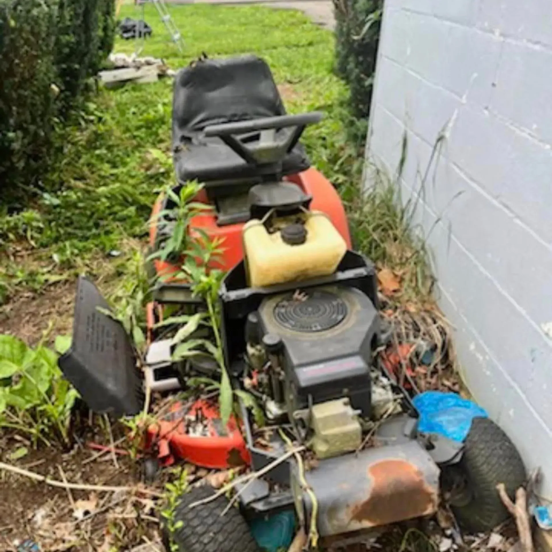 Hall’s Hauling - A lawn mower is sitting in the grass next to a brick wall.