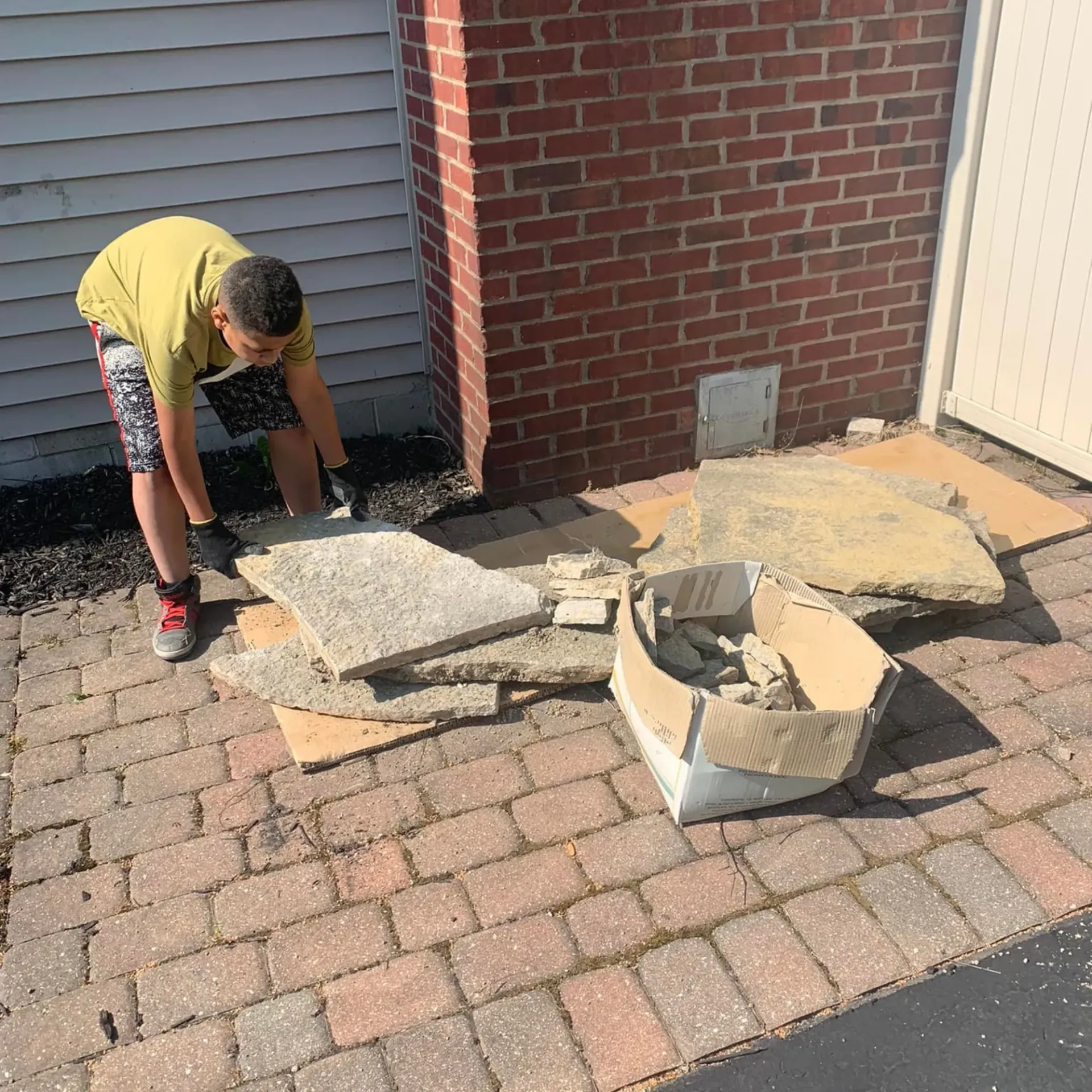 Hall’s Hauling - A boy is kneeling on a brick sidewalk next to a box of bricks.