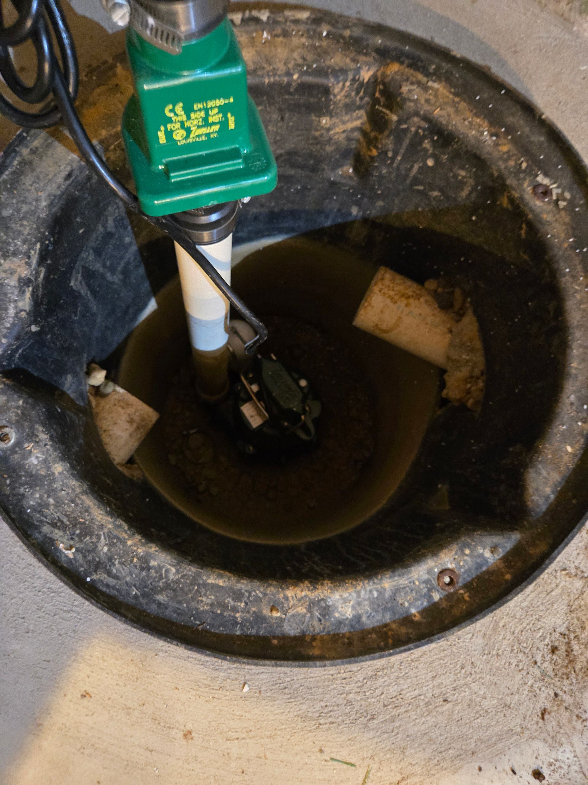 Sump pump in a dark basin with water. A green switch sits on top, with a pump submerged.
