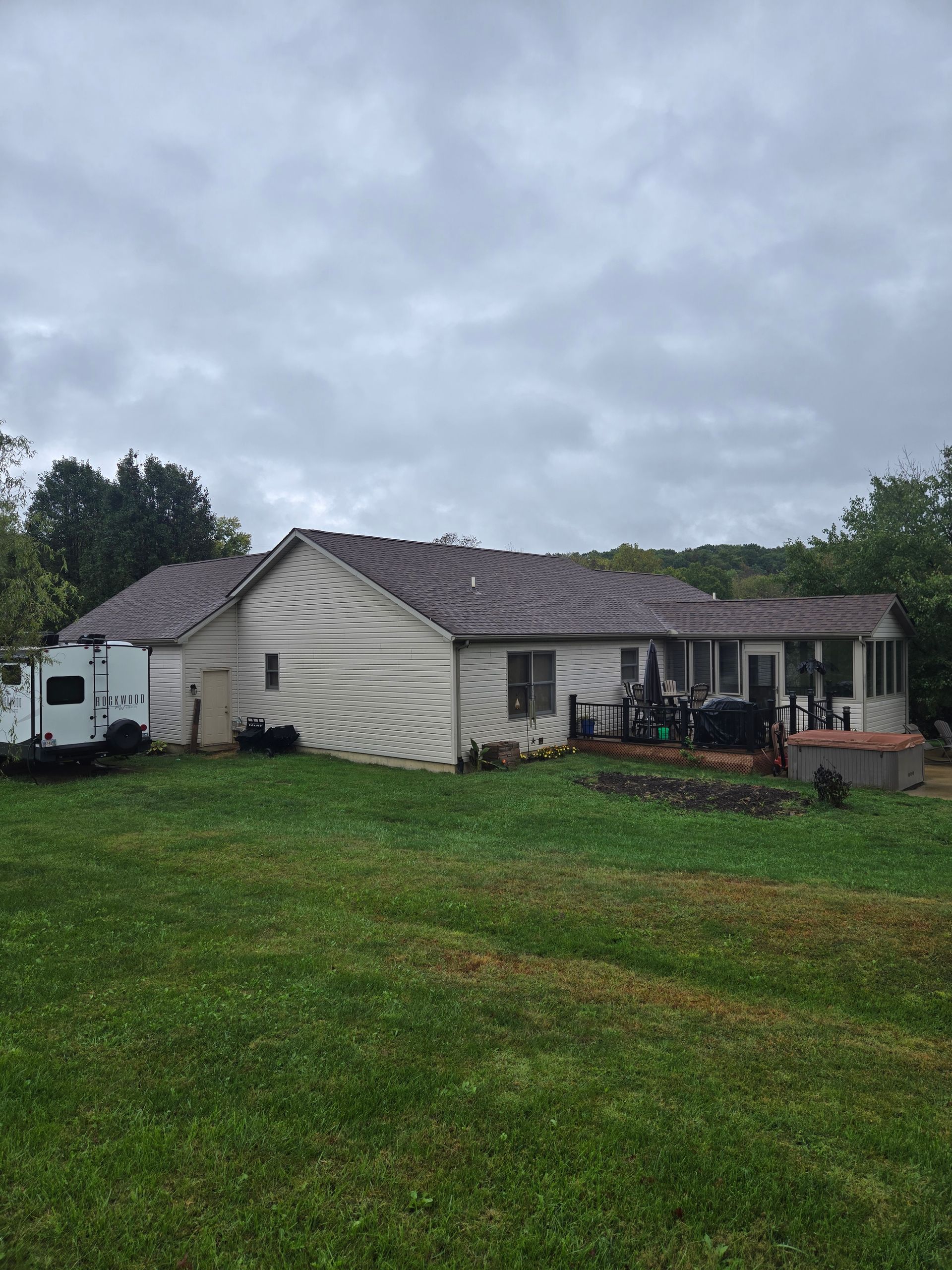 Back of a house with a brown roof and white siding; a grassy lawn and cloudy sky.