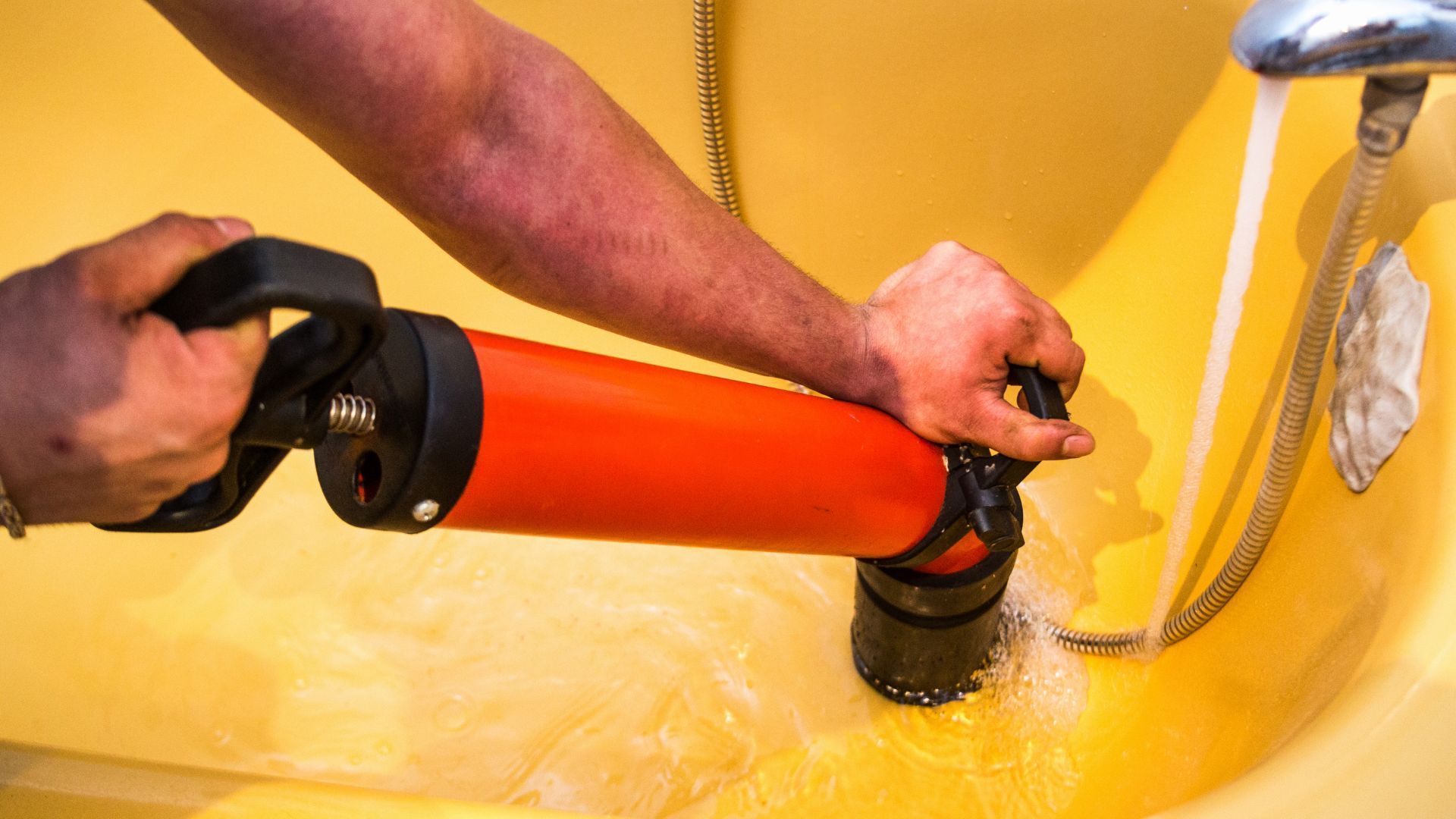 A person is using a plunger to unblock a drain in a bathtub.