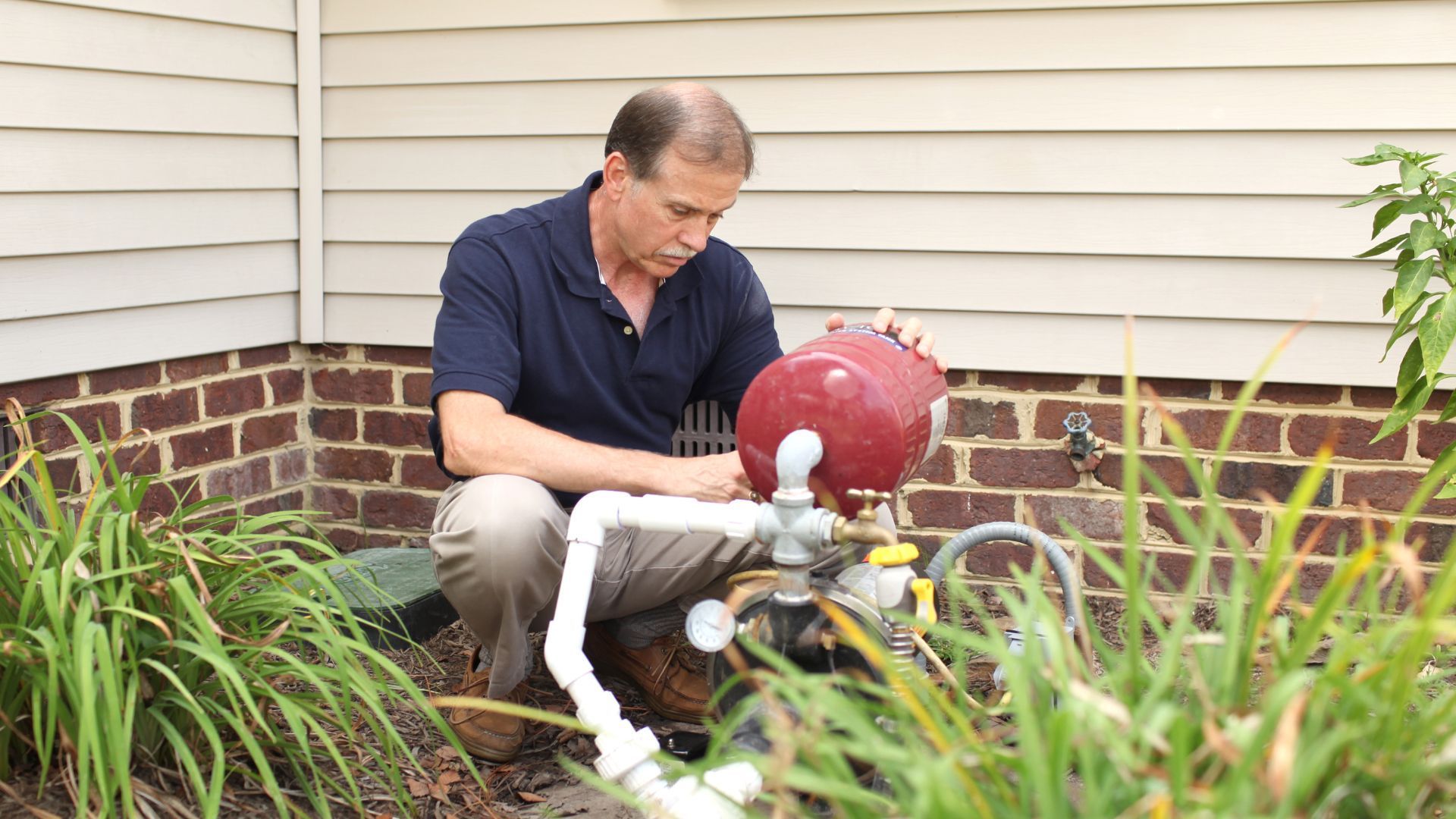 A man is working on a water pump outside of a house.