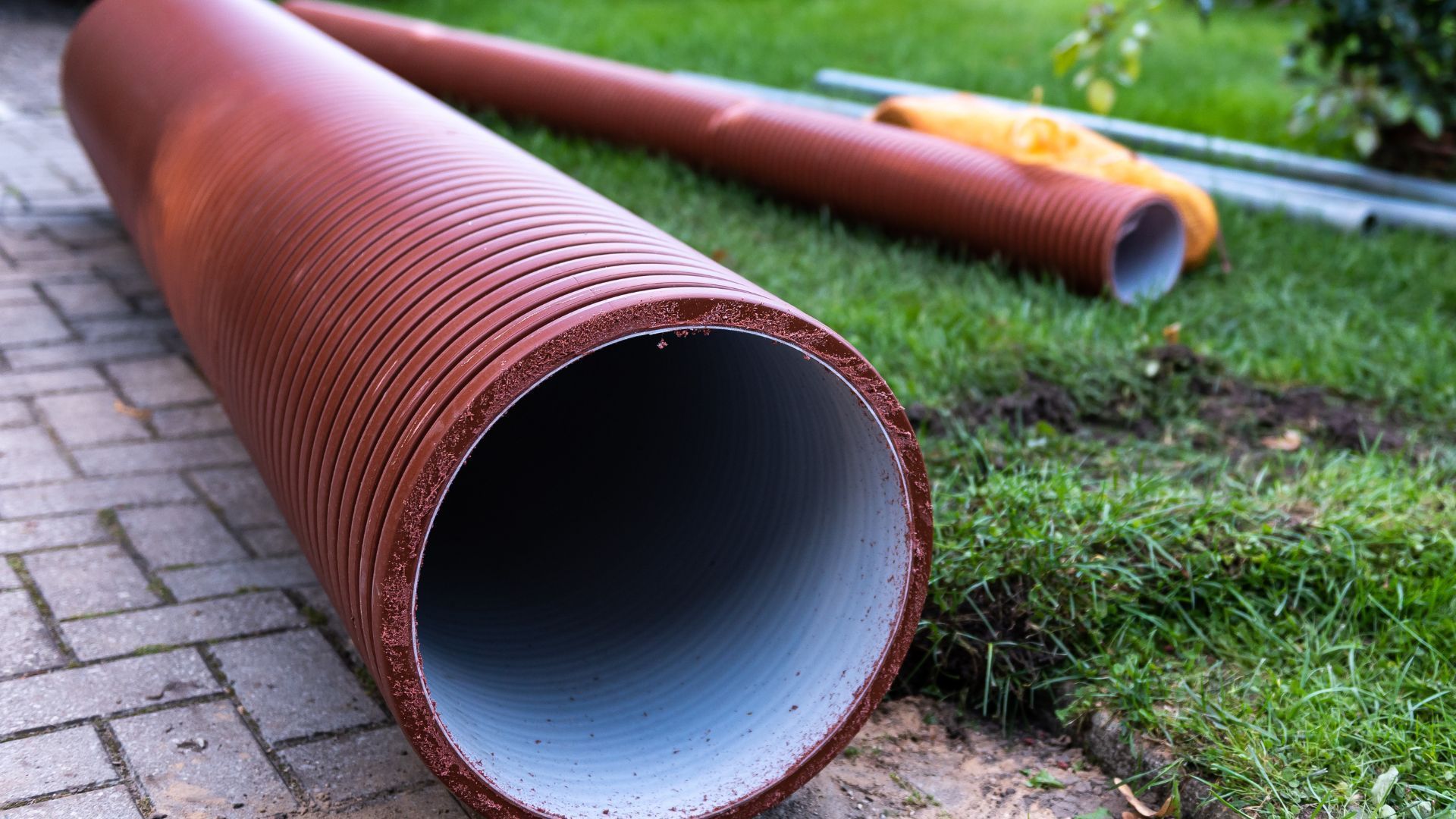 A large red pipe is laying on the ground on a sidewalk.