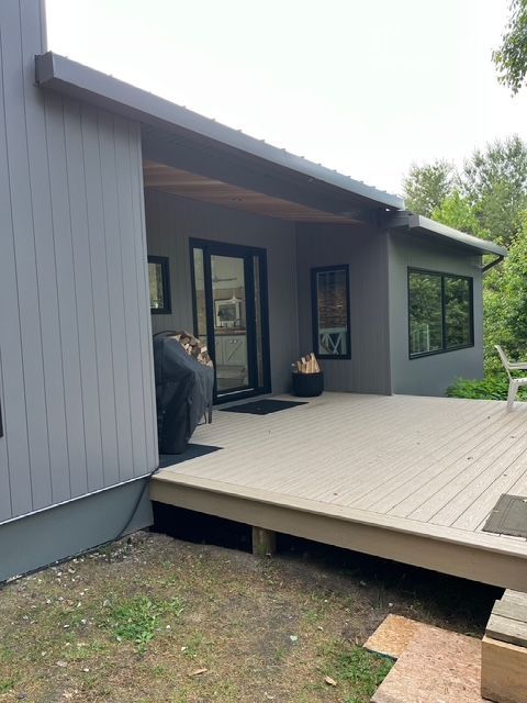 Modern gray house exterior with a raised wooden deck and covered patio entrance