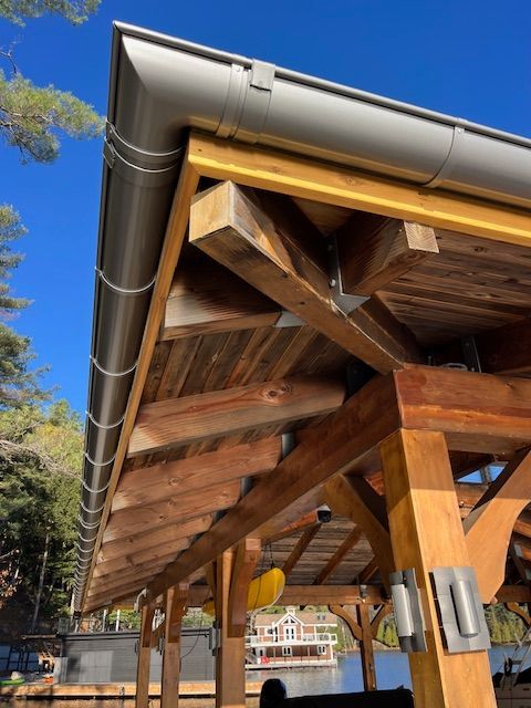 Wooden pavilion with exposed beams and metal roof gutters under a blue sky