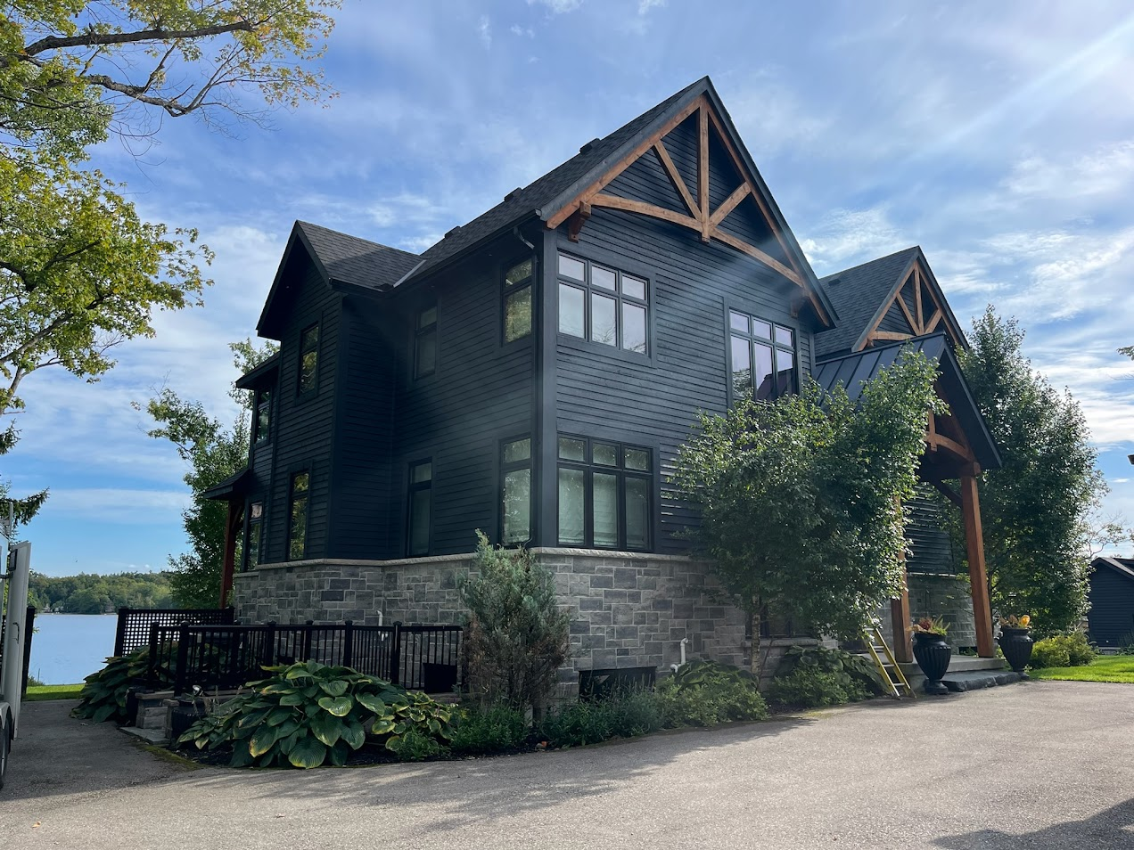 Black house with stone foundation, wooden accents, and a lake view on a sunny day.