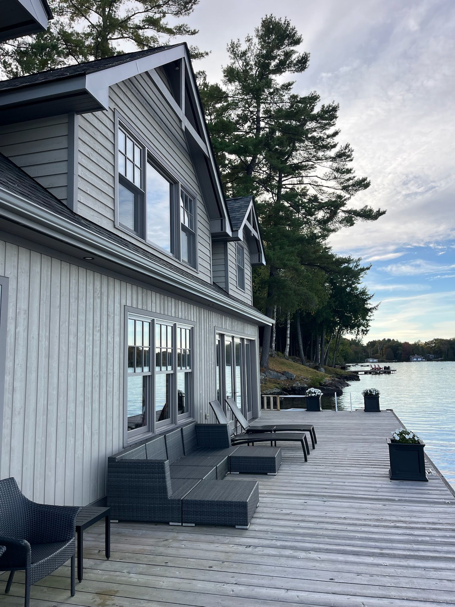 A two-story lakeside home with a wooden dock, gray siding, and large windows.