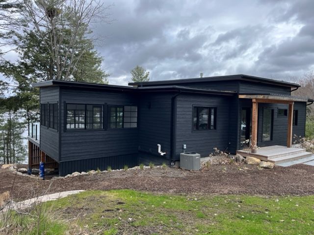 Modern black house exterior on a cloudy day, with large windows and a small porch.