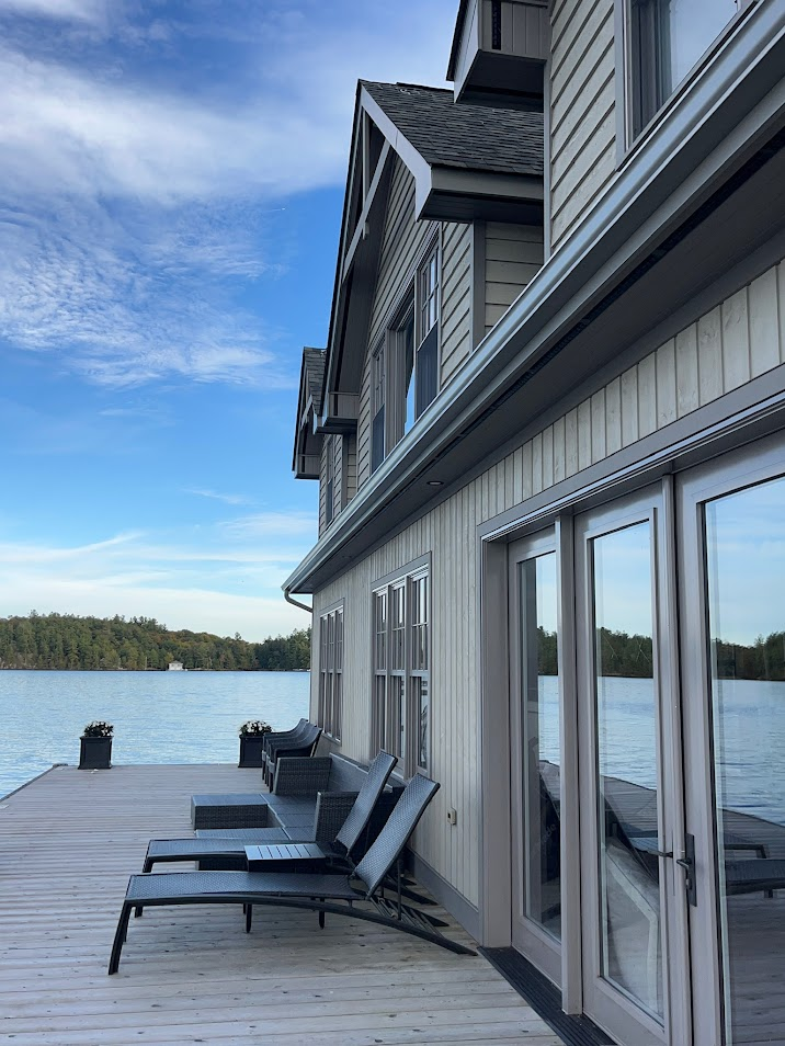 Lakefront home with deck, lounge chairs, and water view under blue sky.