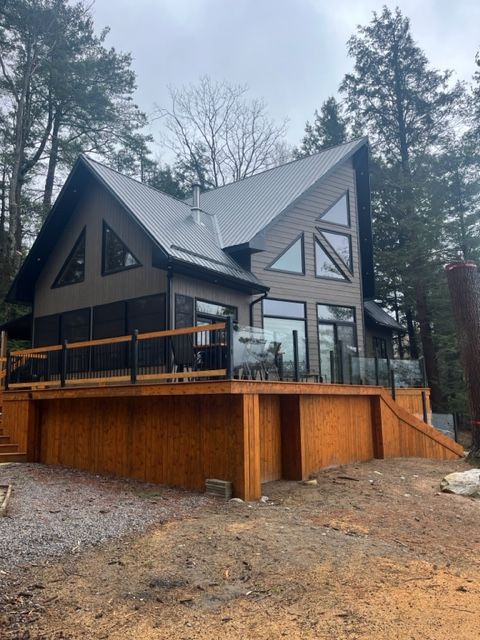 Modern dark-gray cabin with large windows on a wooden deck in a forest setting