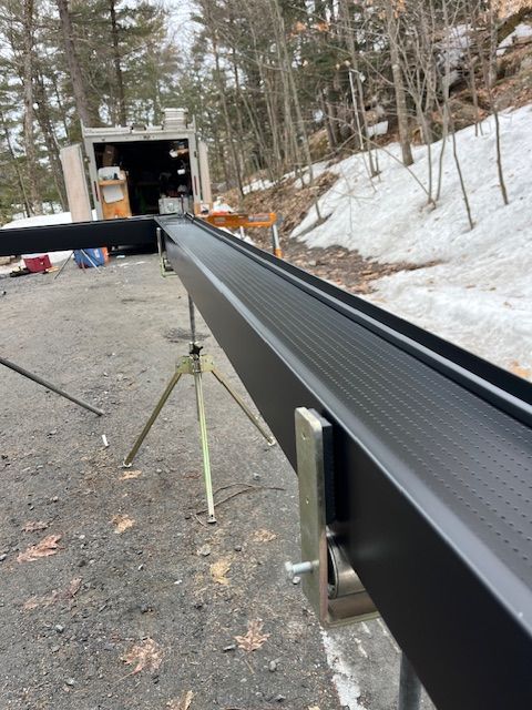 Black conveyor belt extending into a truck loading dock on a snowy roadside worksite