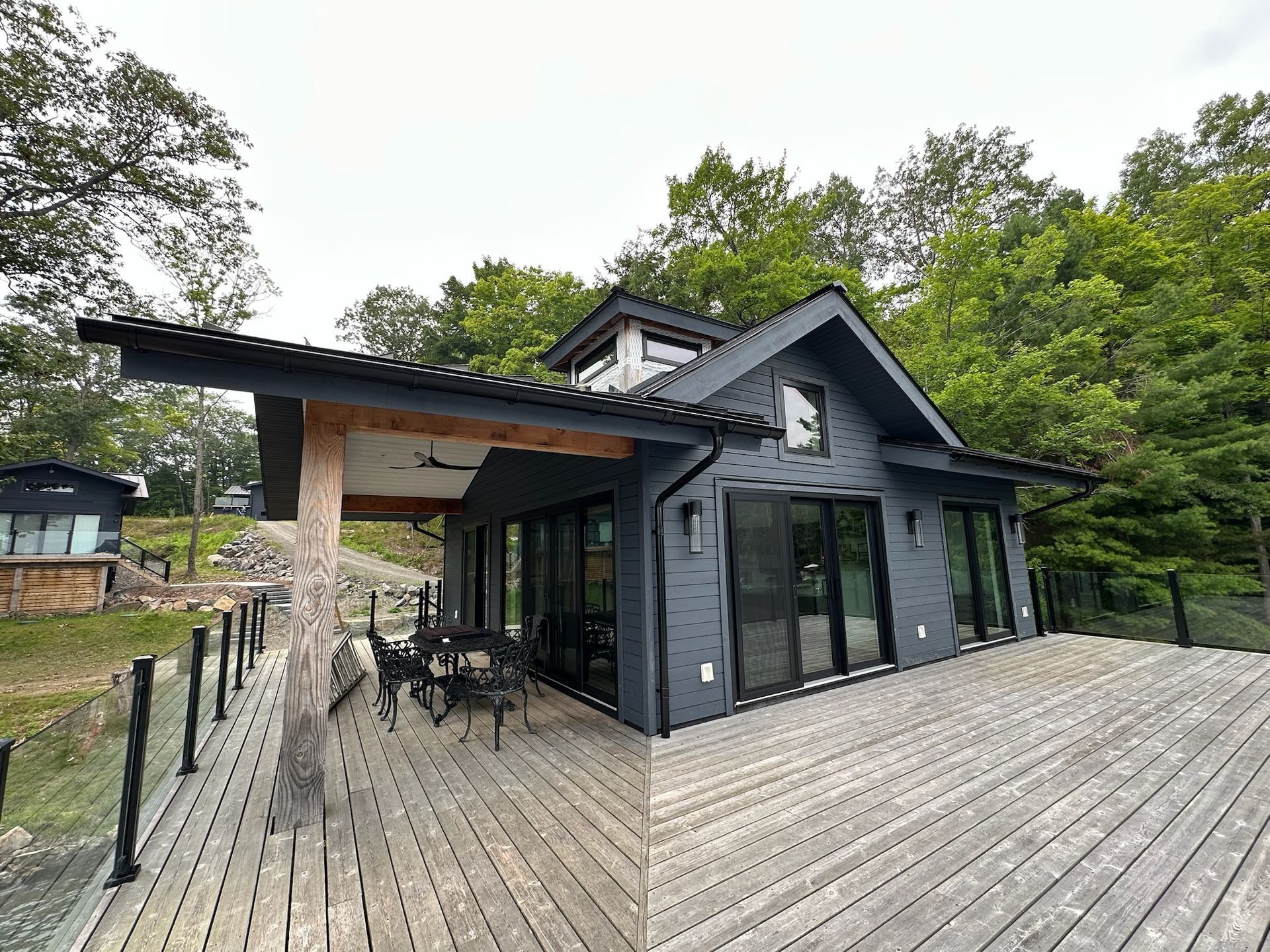 Modern cabin with dark gray siding, deck, and large glass doors, surrounded by trees.