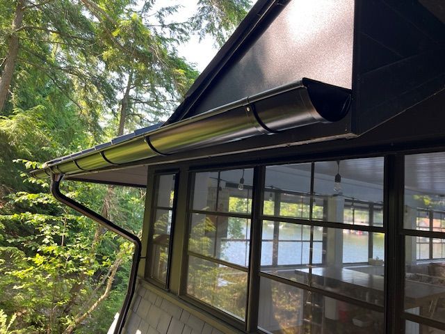 Modern house exterior with black roof, large windows, and forested surroundings