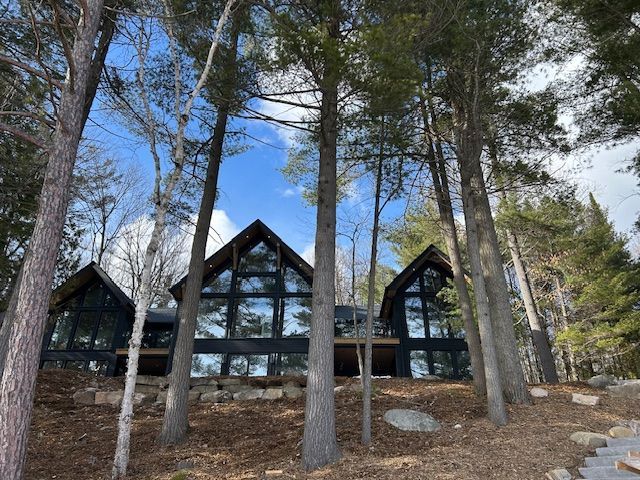 A-frame cabin with large windows among tall pine trees on a wooded hillside
