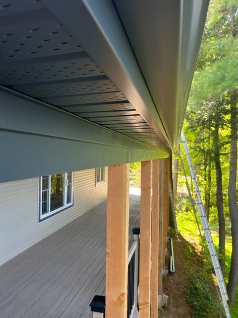 A new home's porch with gray gutters, wood pillars, and a ladder against trees.