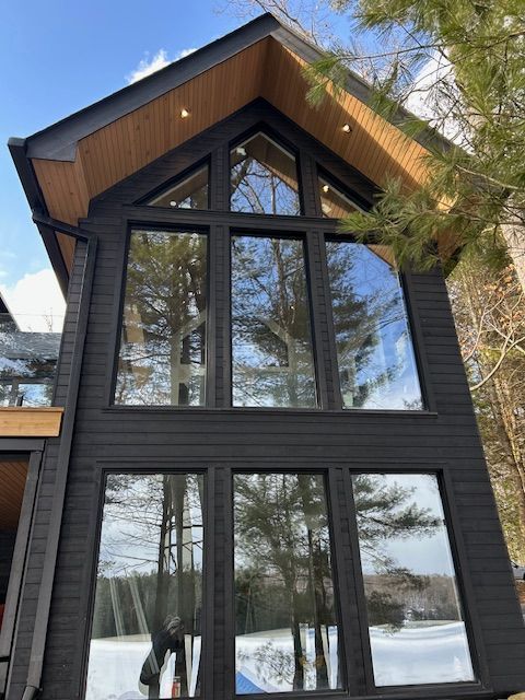 Modern dark house exterior with large windows and steep wooden gable roof in a snowy setting