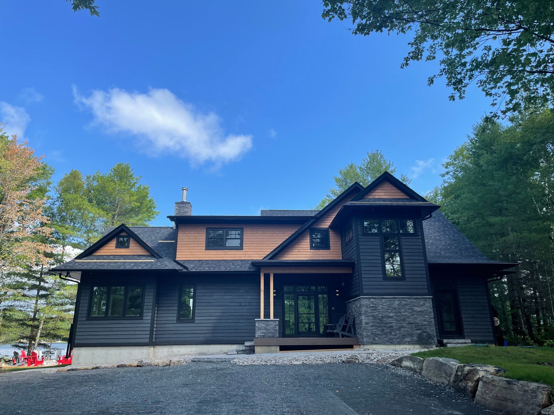 Modern house with black siding, wood accents, and stone facade under a blue sky.