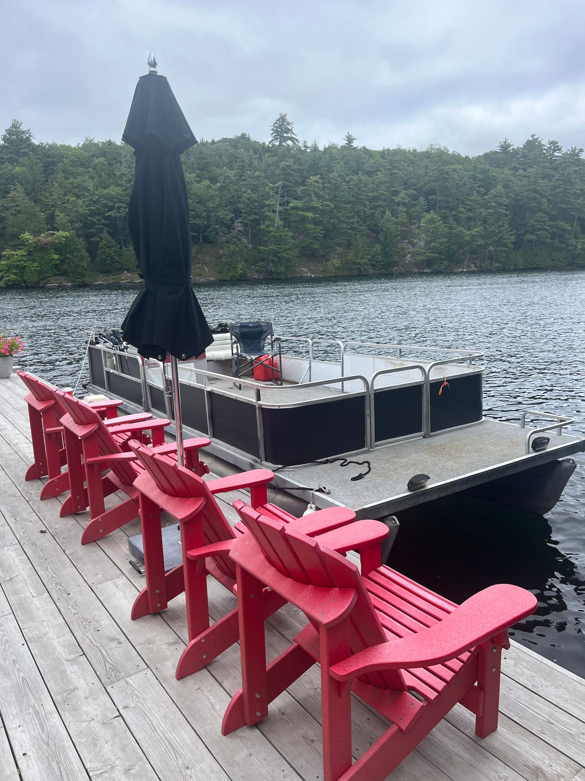 A row of red chairs are sitting on a dock next to a boat.