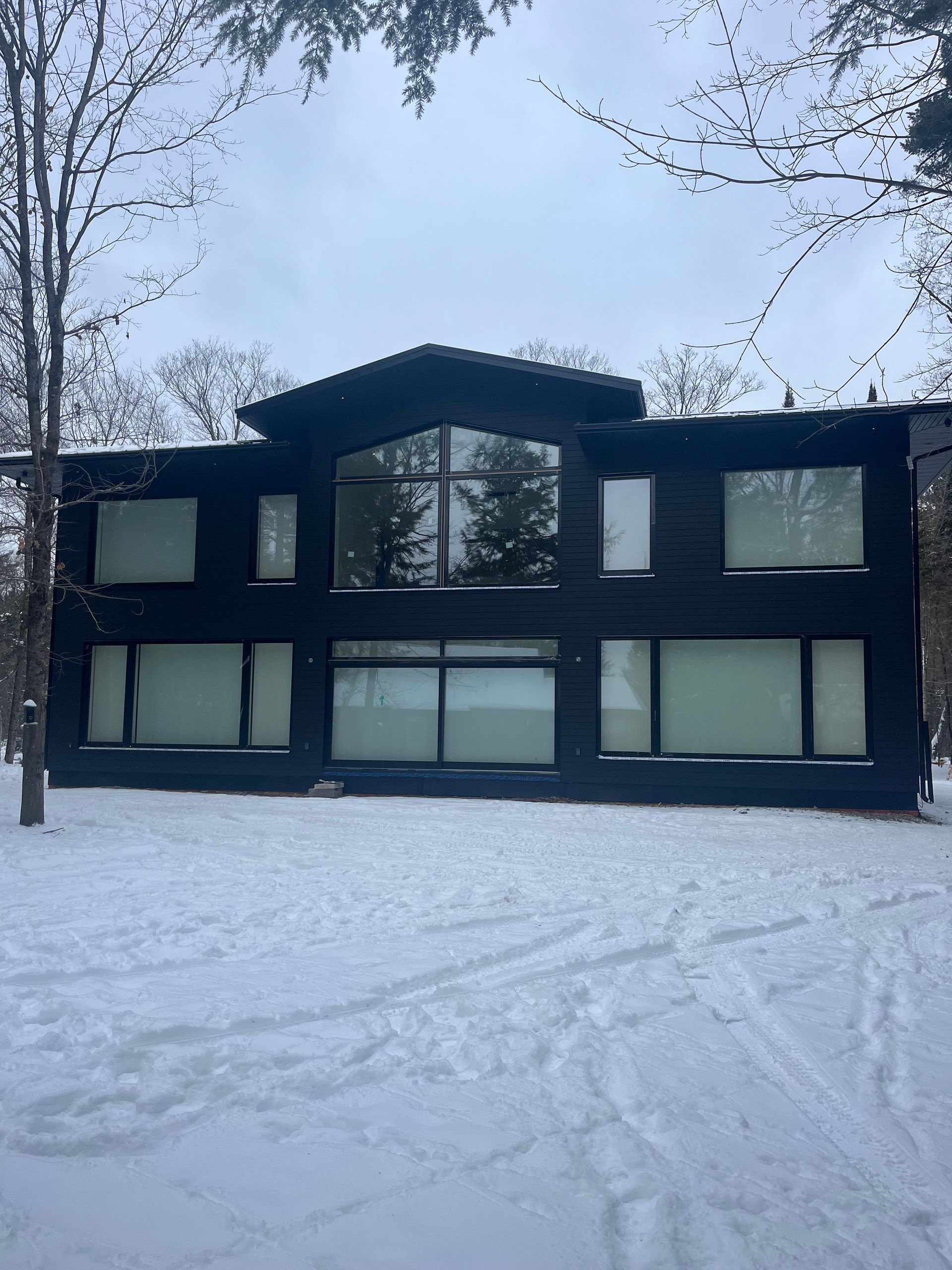 A large black house with a lot of windows is covered in snow.