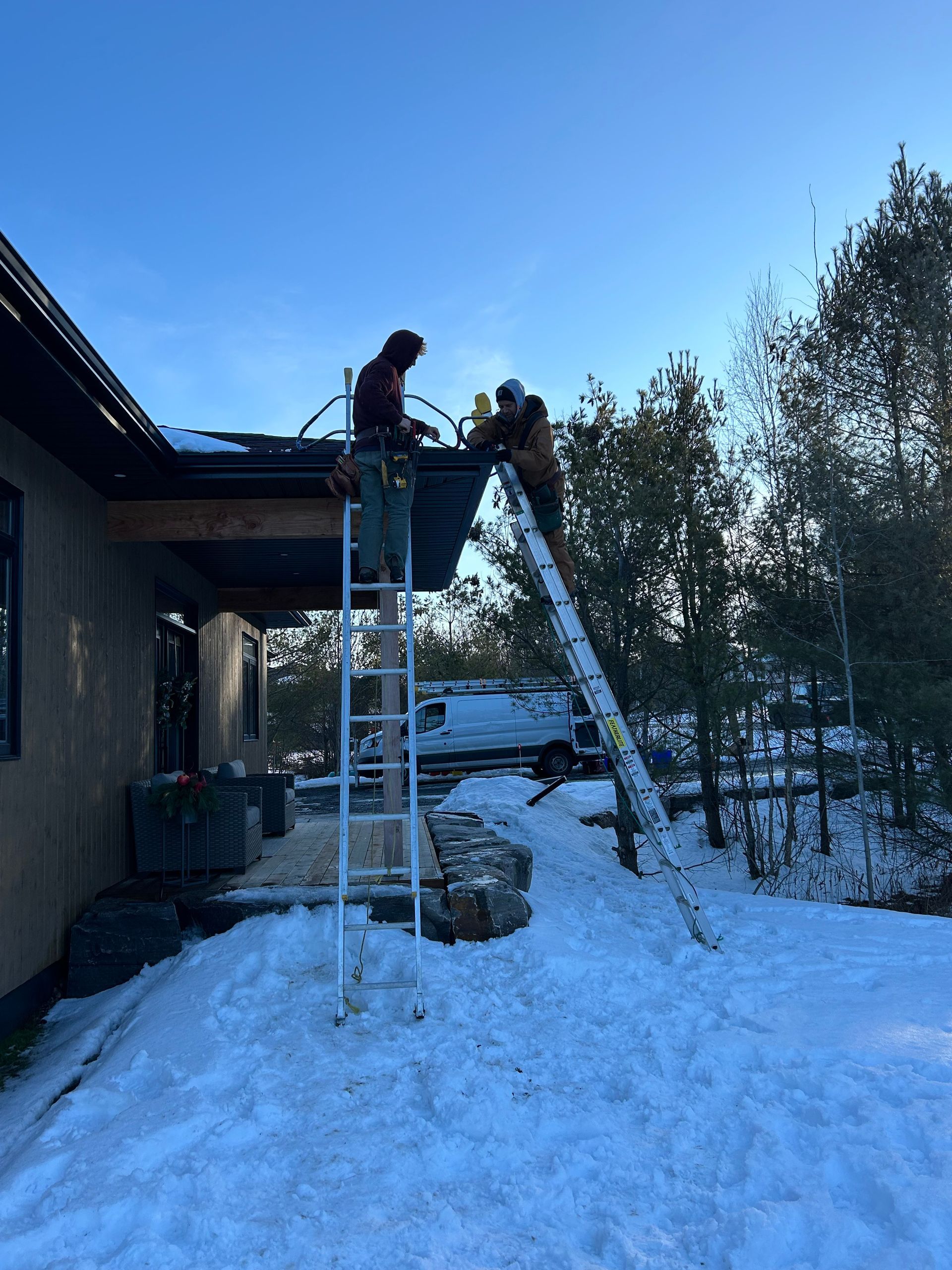 A group of people are working on the roof of a house in the snow.