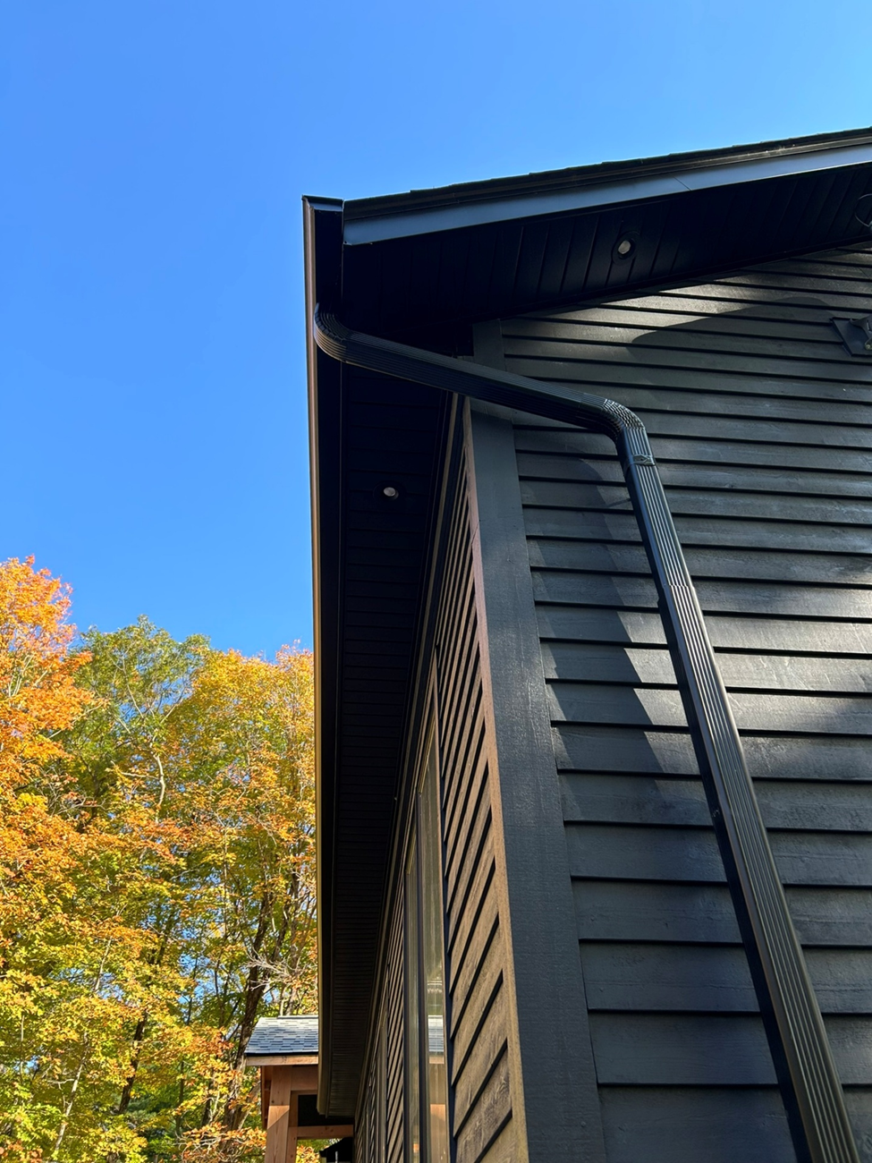 A black house with a gutter on the side of it and trees in the background.