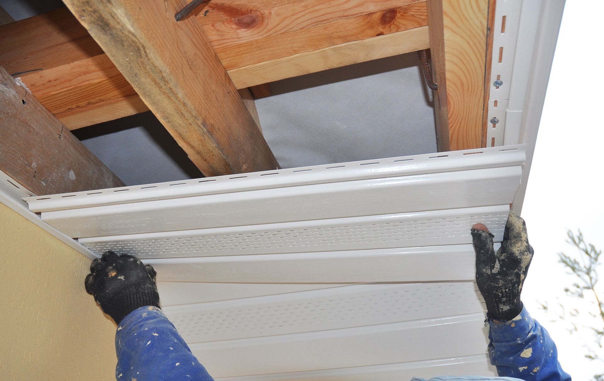 A person is installing siding on the ceiling of a house.