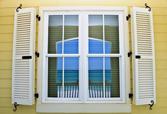 Yellow house window with white shutters, reflecting blue object.