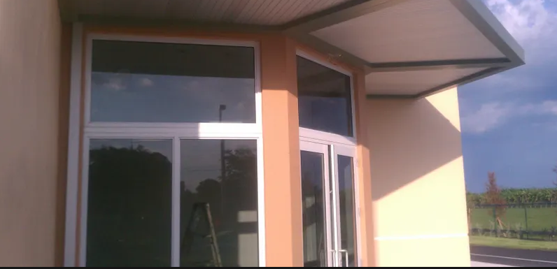 Building exterior with large windows and a covered entrance. Tan walls and a cloudy sky visible.