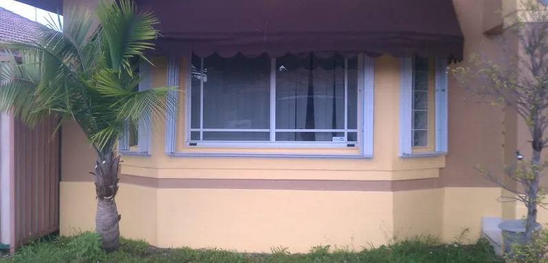 Yellow house with a bay window and awning. A palm tree is in front.