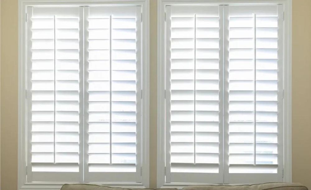 Two white shuttered windows set in a neutral-colored wall.