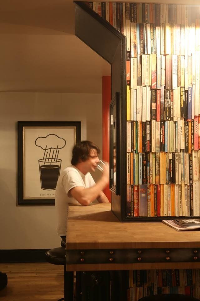 A man drinking from a glass in front of a wall of books