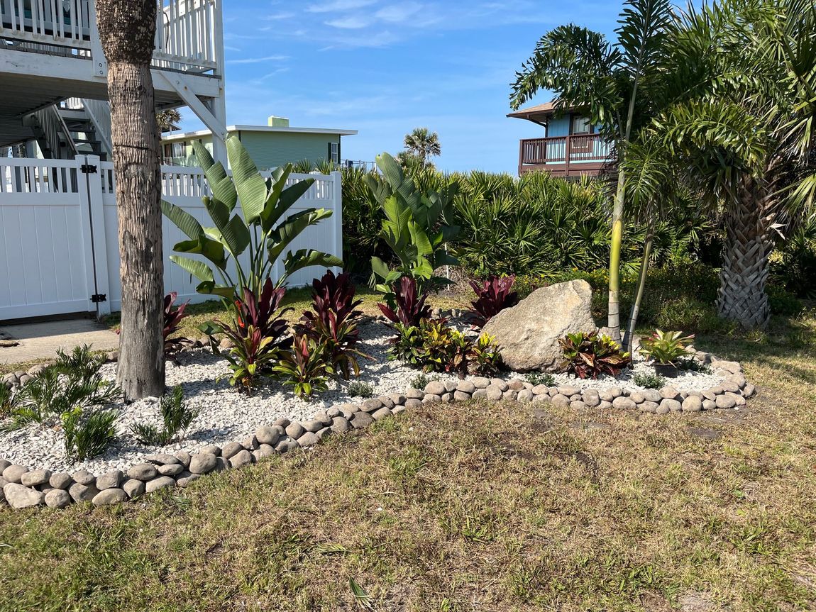 There is a large rock in the middle of a garden in front of a house.