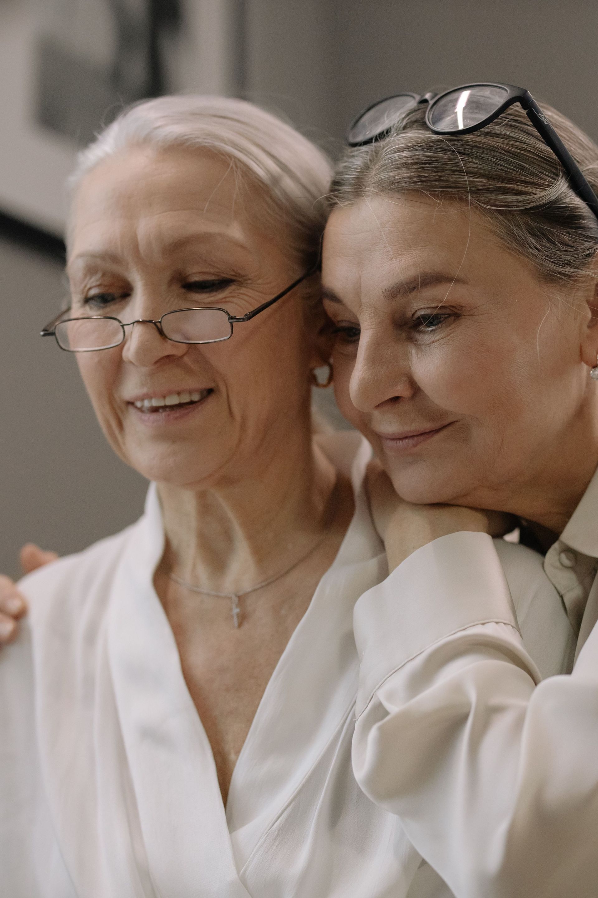 An older person with grey curly hair wearing a white shirt and pearls holding their head with both hands in distress.